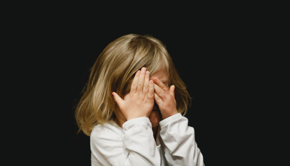 Auch Kinder haben Herausforderungen im Leben. Auf diesem Bild ist ein junges Mädchen zu sehen, das sich mit den Händen die Augen zuhält, als würde es ihre Tränen verstecken wollen.