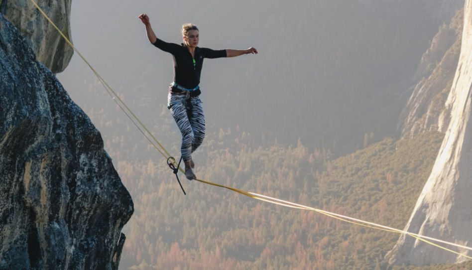 Hier ist eine junge Frau zu sehen, die in luftiger Höhe auf einem Seil balanciert.