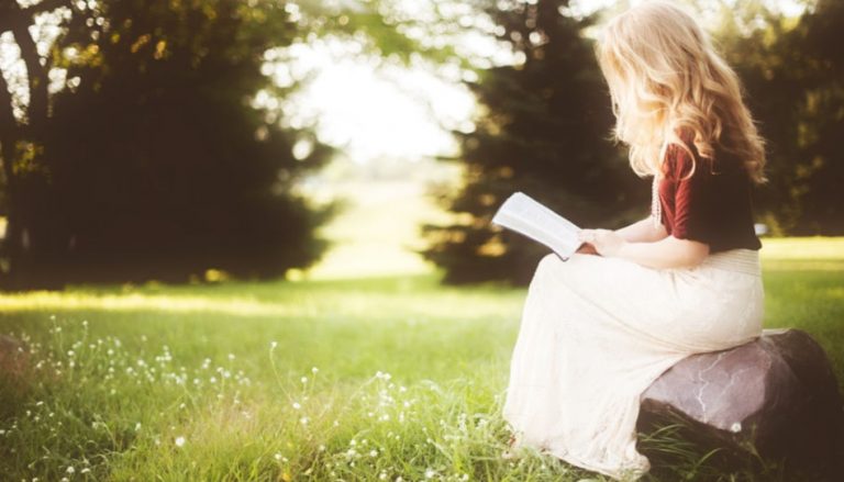 Passend zum Thema "Schöne Bibelzitate" sieht man auf diesem Bild eine junge Frau auf einem Stein sitzend, die in einer Bibel liest.