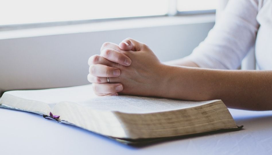 Zu sehen sind zum Beten gefaltete Hände, die auf einer Bibel liegen.