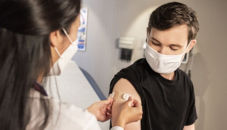 Eine Ärztin klebt ein Pflaster auf den Arm eines zuvor geimpften jungen Mannes.