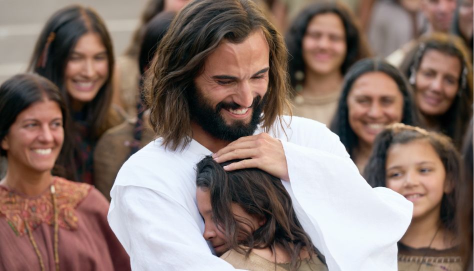 Jesus umarmt ein junges Mädchen und lächelt dabei. Jedes Leben auf der Erde ist ihm wichtig.