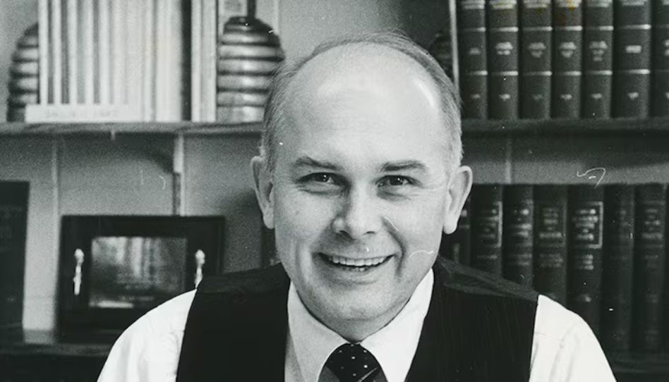 Ein altes Foto von Präsident Oaks, der in seinem Büro sitzt und in die Kamera lächelt.