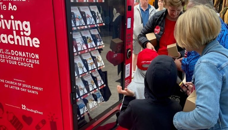 Besucherinnen und Besucher stehen gemeinsam vor einer Giving Machine der Kirche Jesu Christi der Heiligen der Letzten Tage und spenden an wohltätige Organisationen.