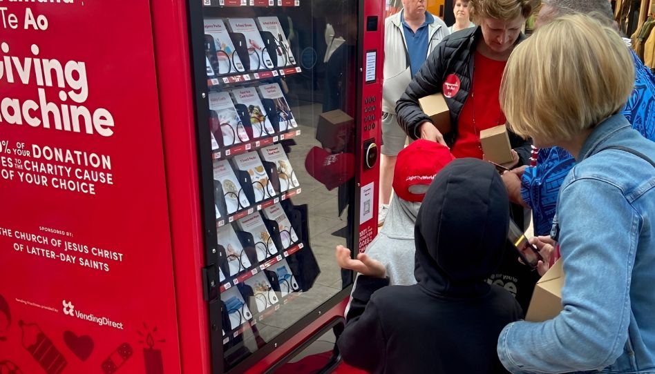 Besucherinnen und Besucher stehen gemeinsam vor einer Giving Machine der Kirche Jesu Christi der Heiligen der Letzten Tage und spenden an wohltätige Organisationen.