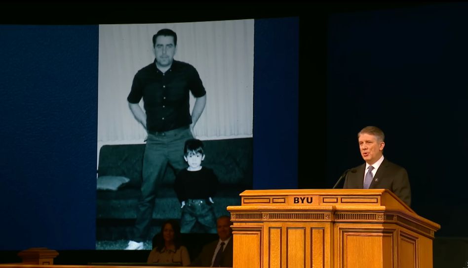 Matthew Holland während einer Ansprache an der BYU. Im Hintergrund ein Foto aus der Kindheit mit seinem Vater. Sie tragen ähnliche Kleidung.