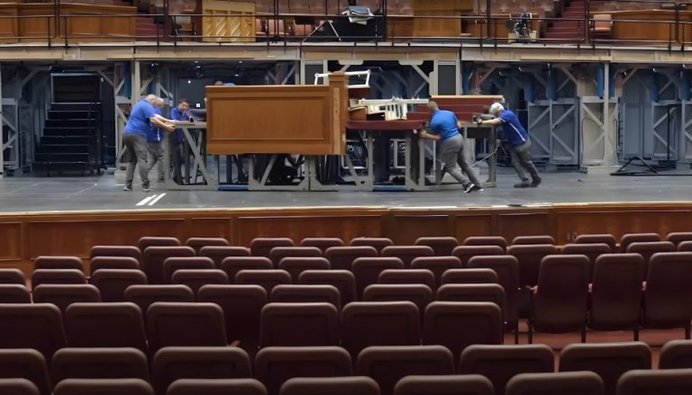EIn paar Männer bauen auf der Bühne der Generalkonferenz etwas auf.