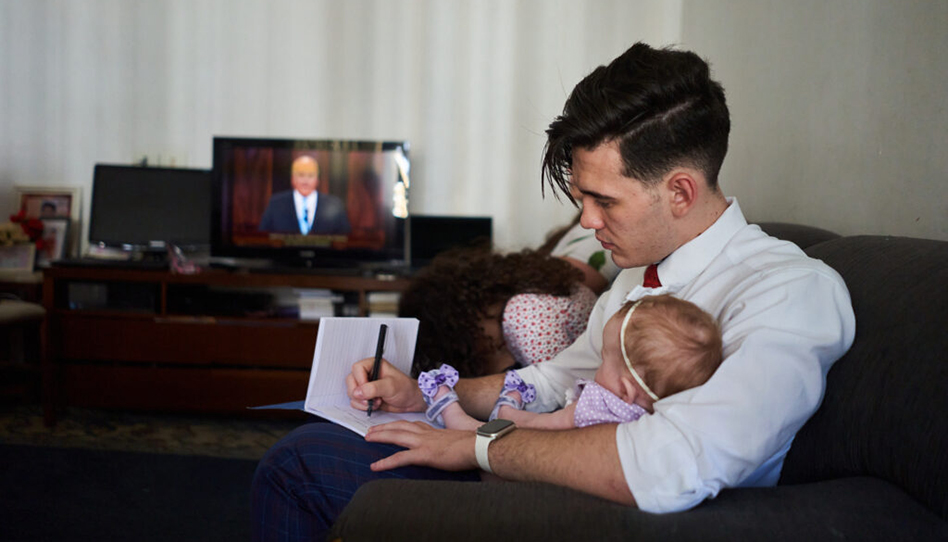 Ein Vater, mit einem Baby auf dem Arm, nimmt Notizen, während er die Generalkonferenz schaut.